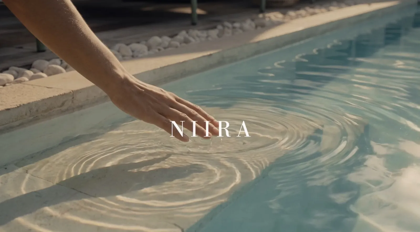 Film frame: a hand touching the pool water under the NiiRA logo.